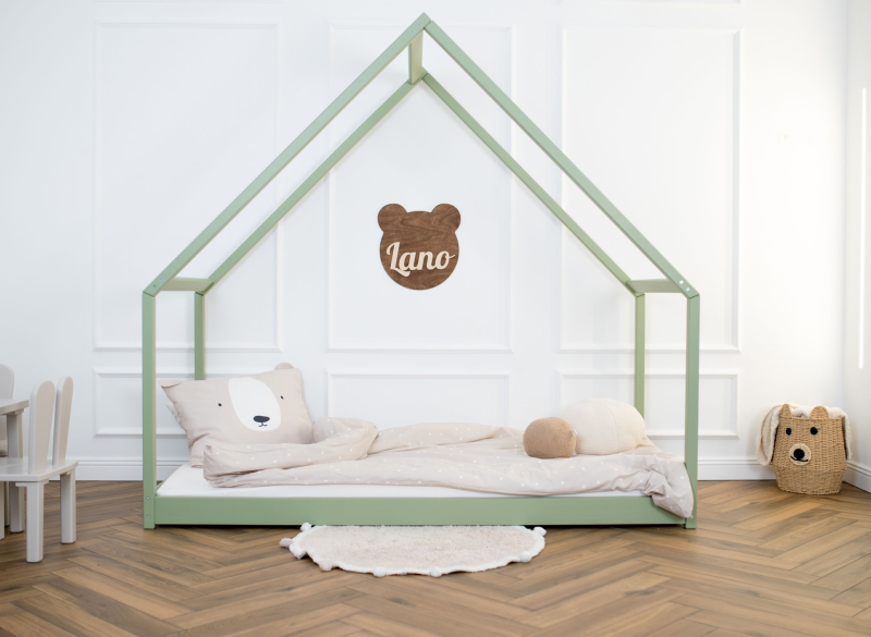 Zielone drewniane łóżko domek dla dziecka, z beżową pościelą, w jasnym pokoju z białymi ścianami.