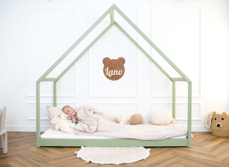 Dziecko śpi w przytulnym, zielonym łóżku w kształcie domku.