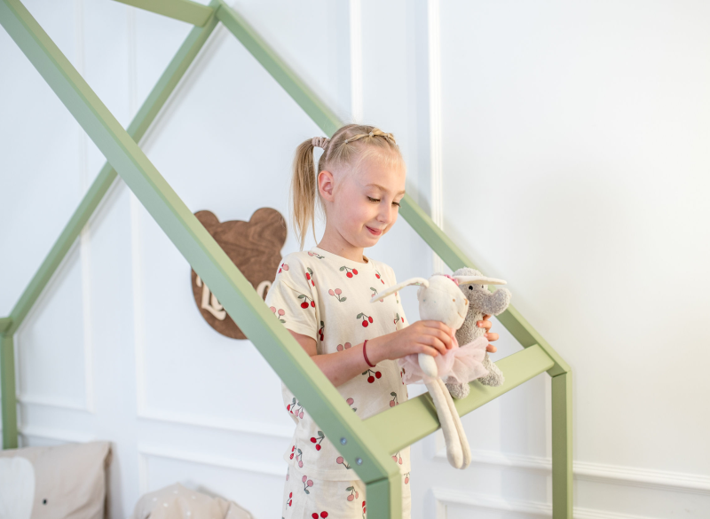 Dziewczynka bawi się przy zielonym drewnianym łóżku domku.