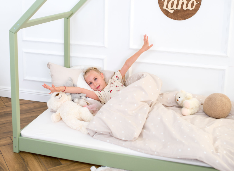 Dziecko budzące się w zielonym łóżku domek z drewna, z beżową pościelą i zabawkami, w jasnym pokoju.