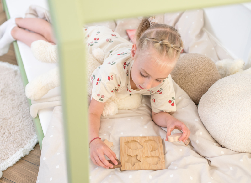 Zbliżenie na dziecko układające drewniane klocki na łóżku domku w pokoju dziecięcym.