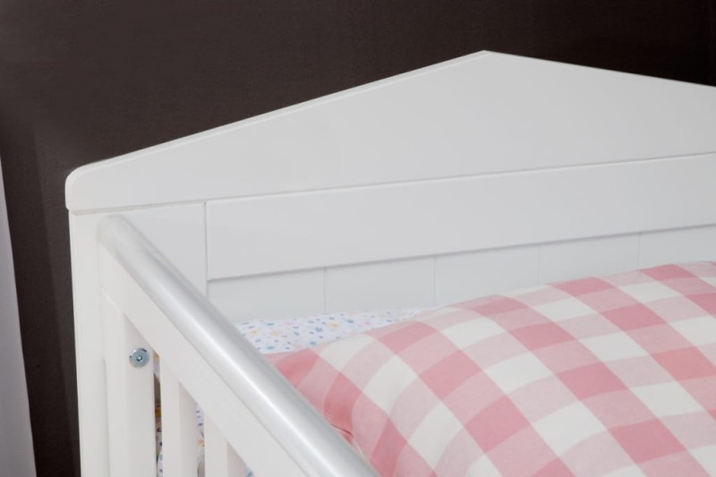 Zbliżenie na białe łóżeczko dziecięce z różową poduszką w kratkę.