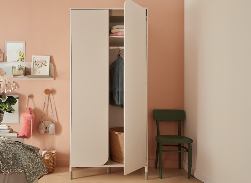 Beżowa szafa dwudrzwiowa z otwartymi drzwiami, zielone krzesło, w pokoju z różową ścianą.