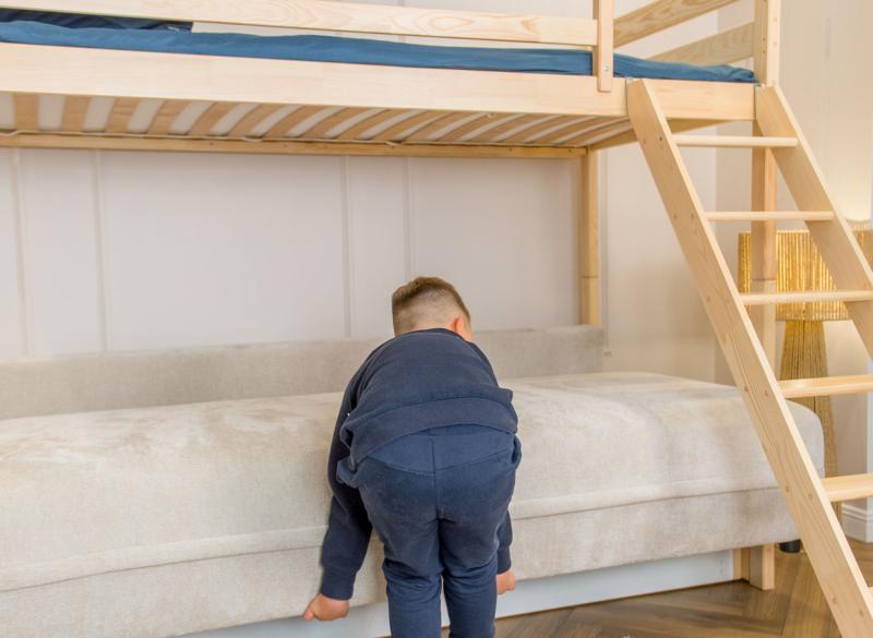 Chłopiec wspina się na sofę pod drewnianym łóżkiem antresolą.