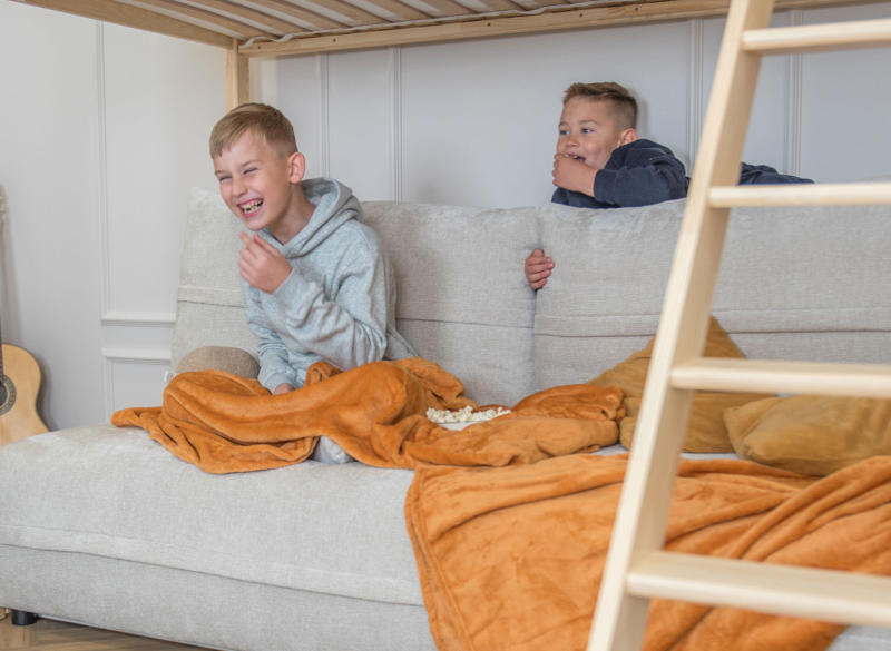 Śmiejące się dzieci na jasnej sofie pod drewnianym łóżkiem piętrowym.
