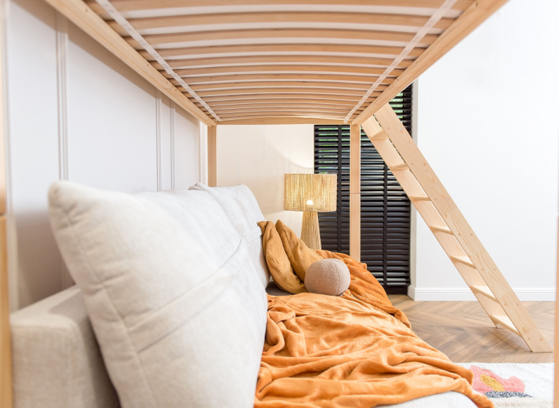 Wnętrze pokoju dziecięcego z widokiem na sofę pod łóżkiem antresolą.