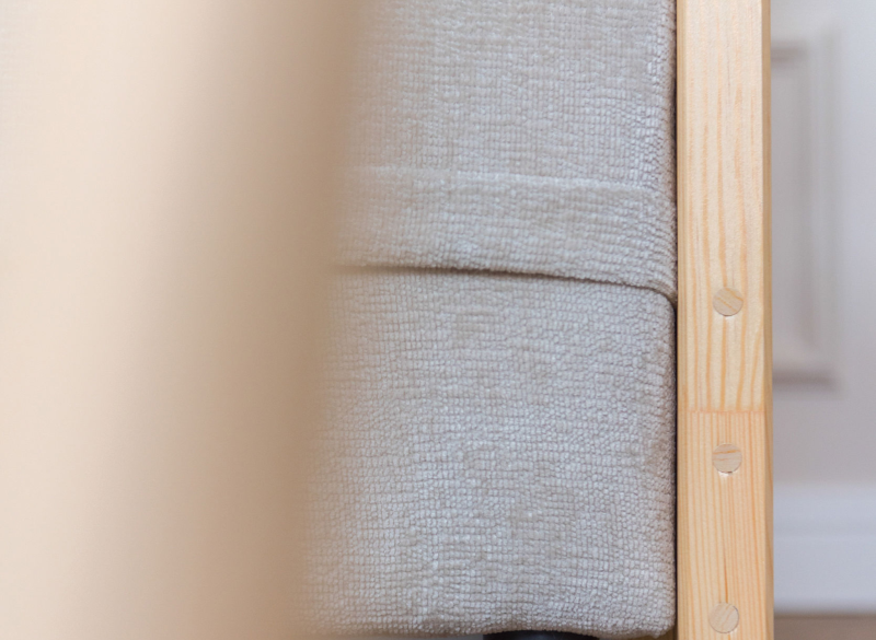 Materac z jasnoszarego, teksturowanego materiału obok drewnianej ramy, widoczne detale konstrukcji.