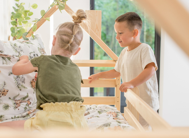 Dwoje dzieci bawiących się na górnym posłaniu drewnianego łóżka domek.