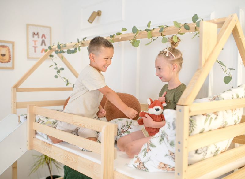 Szczęśliwe dzieci siedzące na piętrowym łóżku domek z miękką pościelą.