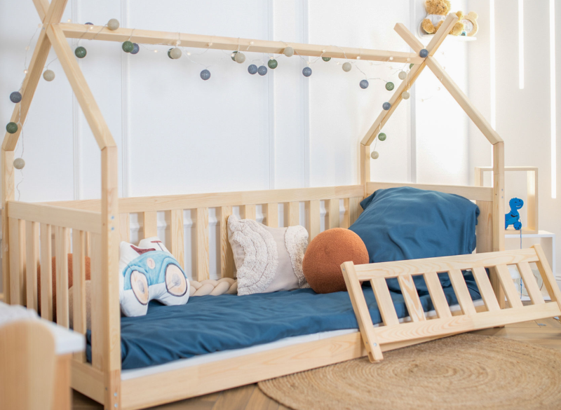 Łóżko domek z drewna dla dzieci z dekoracyjnymi lampkami i błękitną pościelą w pokoju.