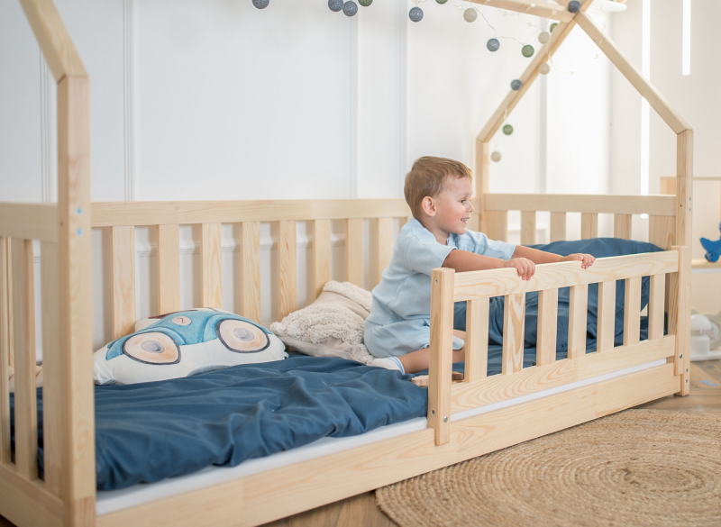 Mały chłopiec bawiący się w bezpiecznym łóżku domek z drewnianymi barierkami.