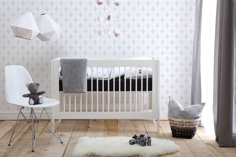 Białe łóżeczko niemowlęce w nowoczesnym pokoju dziecięcym z dekoracjami.