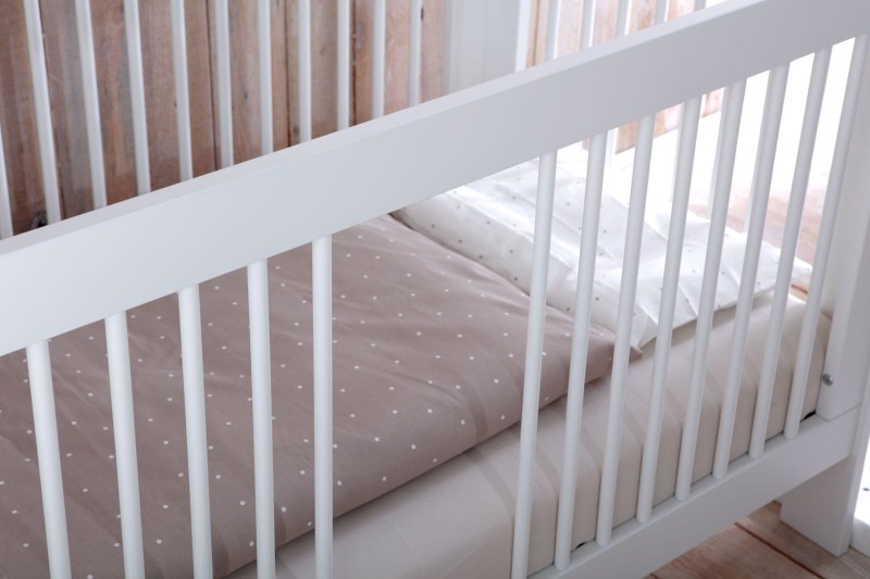 Zbliżenie na bawełnianą pościel w kropki wewnątrz białego łóżeczka.