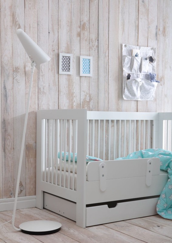 Białe drewniane łóżeczko dziecięce z barierką ochronną w przytulnym pokoju.