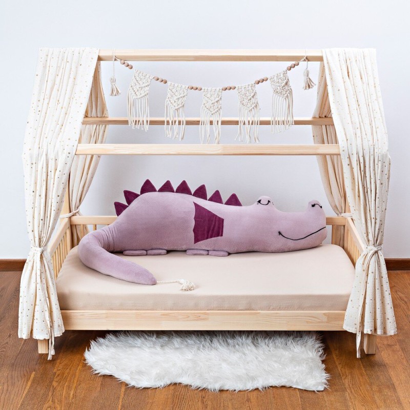 Drewniane łóżko domek dla dziecka z dużym, fioletowym pluszowym smokiem i białym dywanikiem.