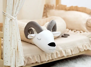 Poduszka dekoracyjna w kształcie barana z rogami na pościeli w pokoju dziecięcym.