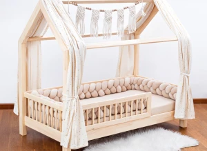 Łóżko domek z drewna z beżowym ochraniaczem warkoczem i dekoracjami.