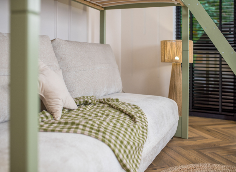 Sofa pod antresolą z zielonym kocem w kratę i lampą w przytulnym pokoju.