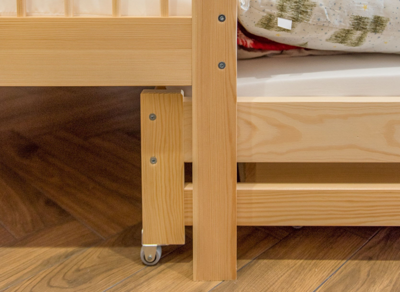 Detale wykończenia drewnianego łóżka dziecięcego na kółkach.