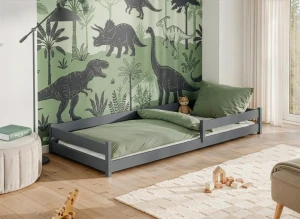 Szare łóżko parterowe dla dziecka w nowoczesnym pokoju z dinozaurami.