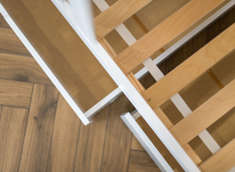 Zbliżenie na drewniany stelaż pod materac w białej ramie łóżka dziecięcego.