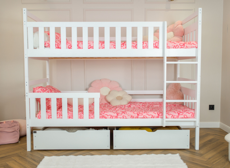 Białe dwupiętrowe łóżko dziecięce z szufladami i różową pościelą w kokardki.