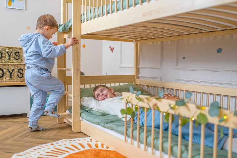 Radosna zabawa rodzeństwa na drewnianym łóżku piętrowym z drabinką.