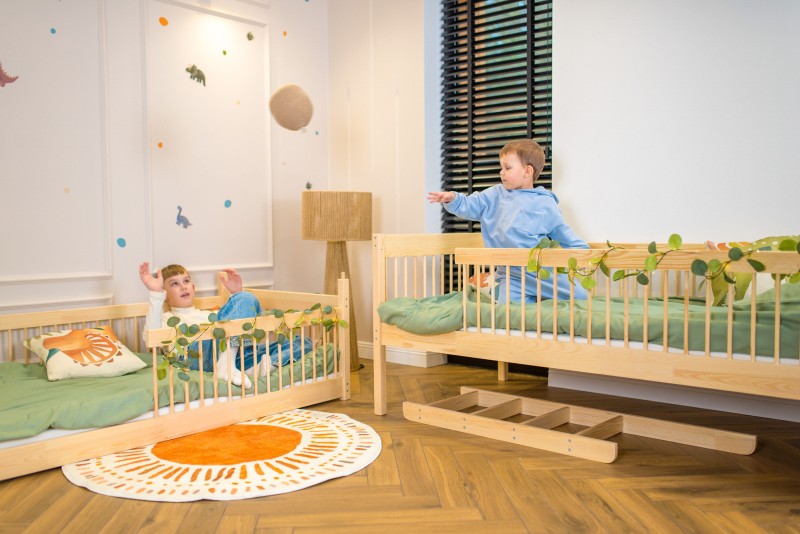 Dwaj chłopcy rzucający piłką, siedząc na oddzielnych drewnianych łóżkach dziecięcych.