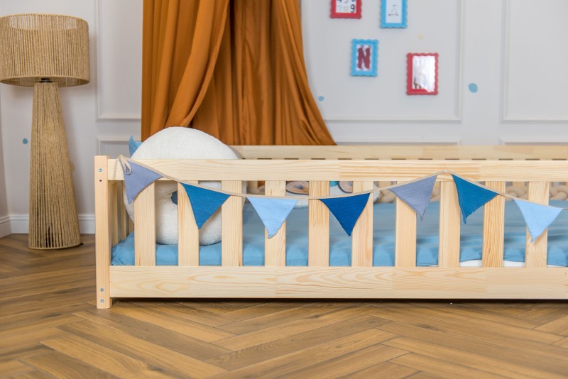 Barierka drewnianego łóżka dziecięcego z ozdobną girlandą z niebieskimi proporczykami.