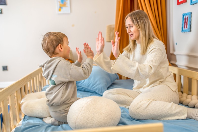 Mama i dziecko bawią się na drewnianym łóżku, przybijając piątkę w przytulnym pokoju.