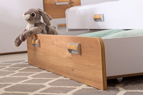 Szuflada pod łóżko z drewnianym frontem i ozdobnymi uchwytami w pokoju dziecięcym.