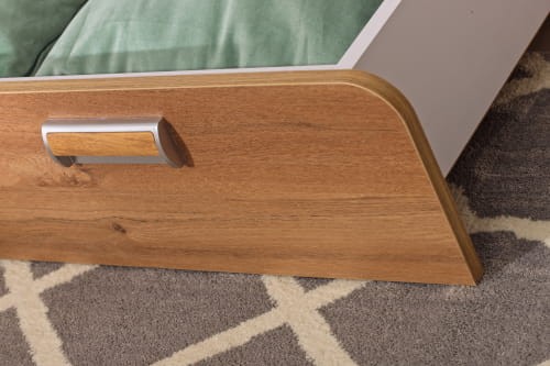 Zbliżenie na drewniany front szuflady łóżka z nowoczesnym, srebrno-drewnianym uchwytem.